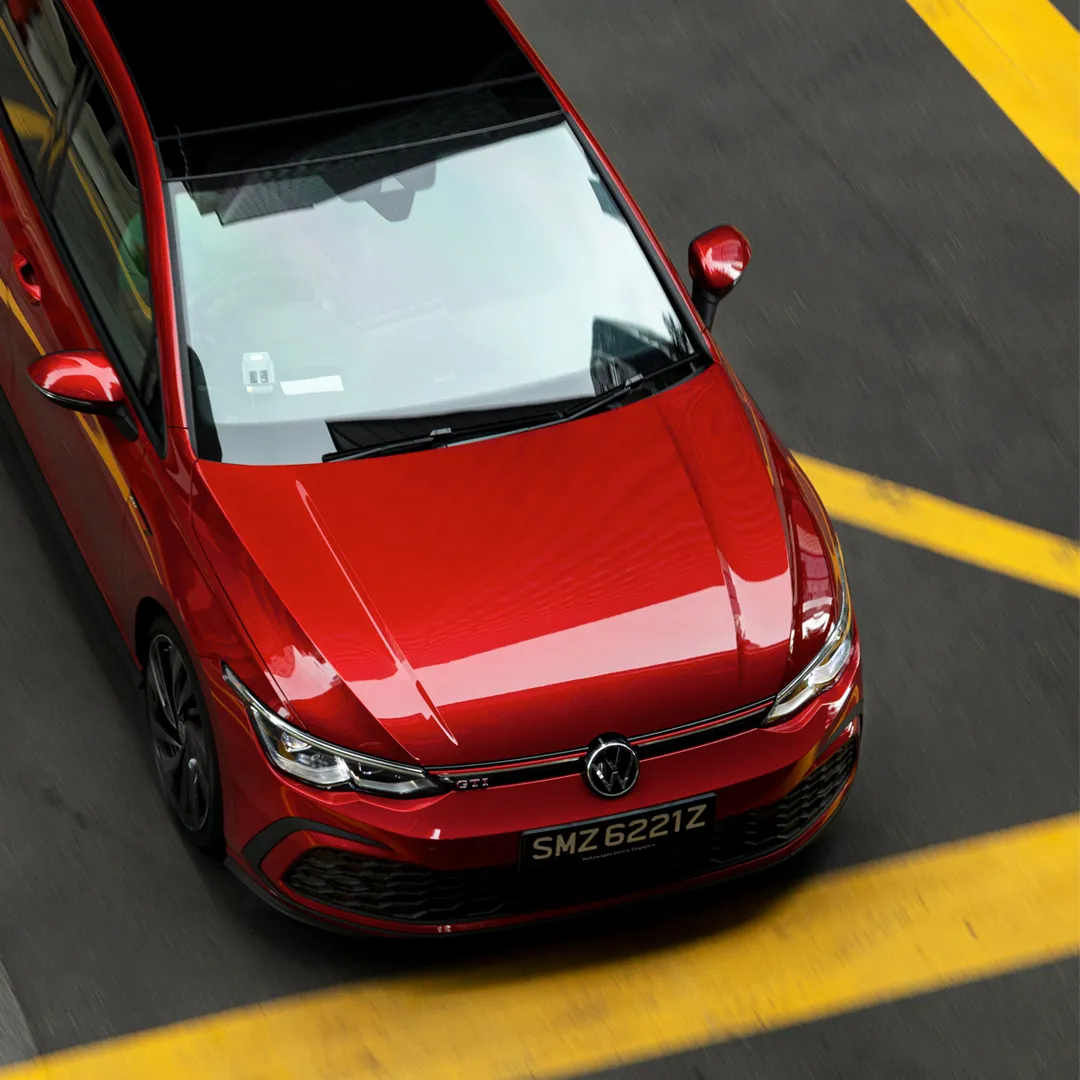 An aerial view of a red Volkswagen GTI cruising past a road with yellow line markings.