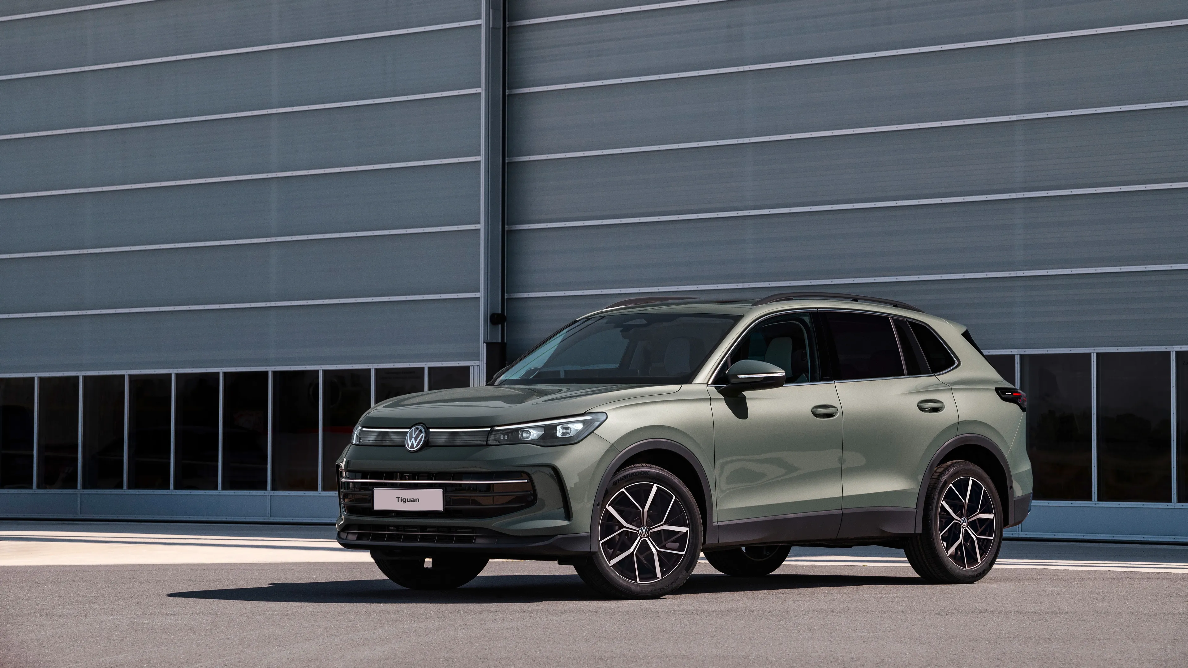 A metallic green Volkswagen Tiguan parked outside an industrial hanger at day.