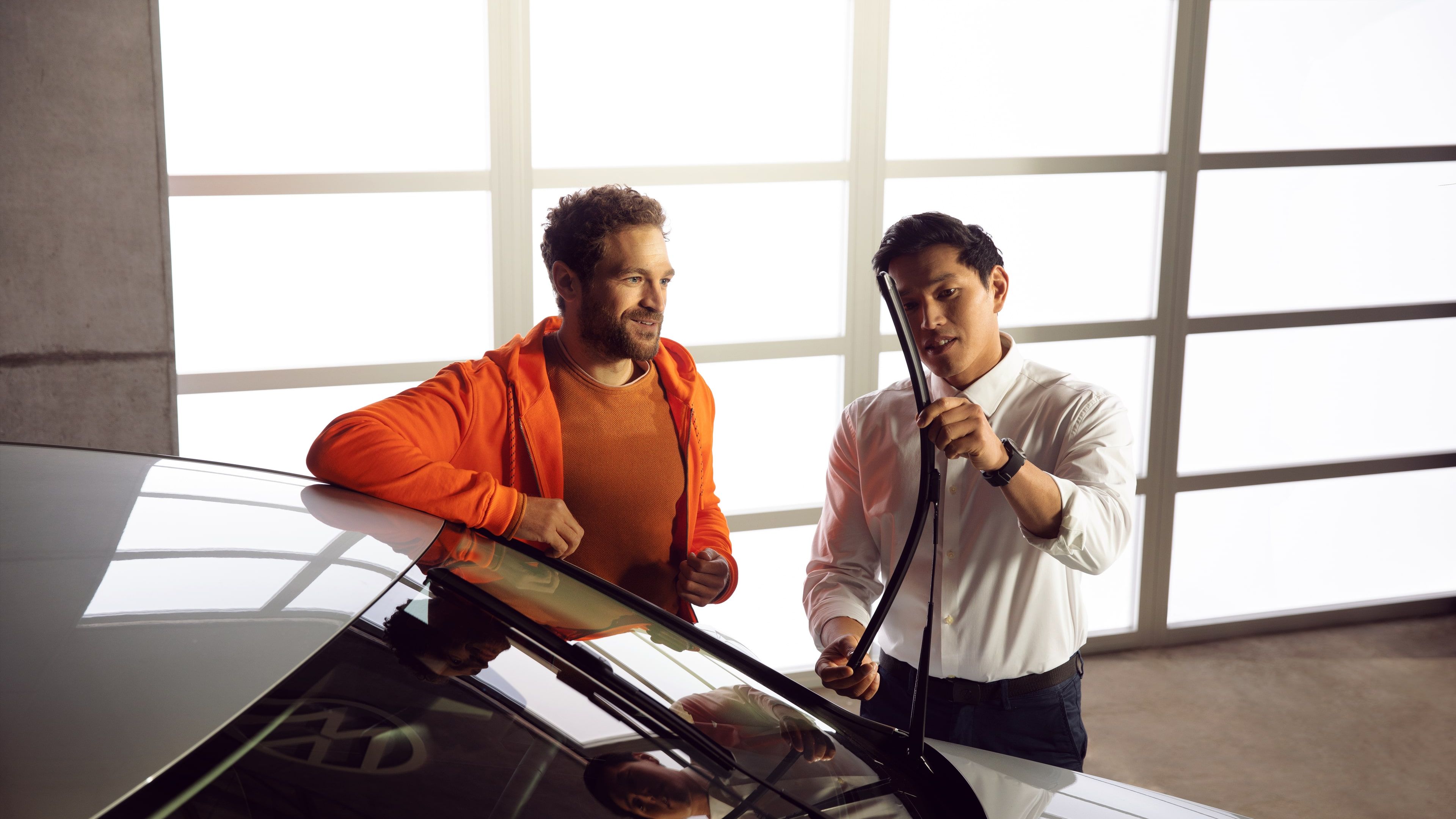 A customer dressed in an orange outfit consulting a Certified Volkswagen Staff about vehicle windscreen wipers at a service centre.