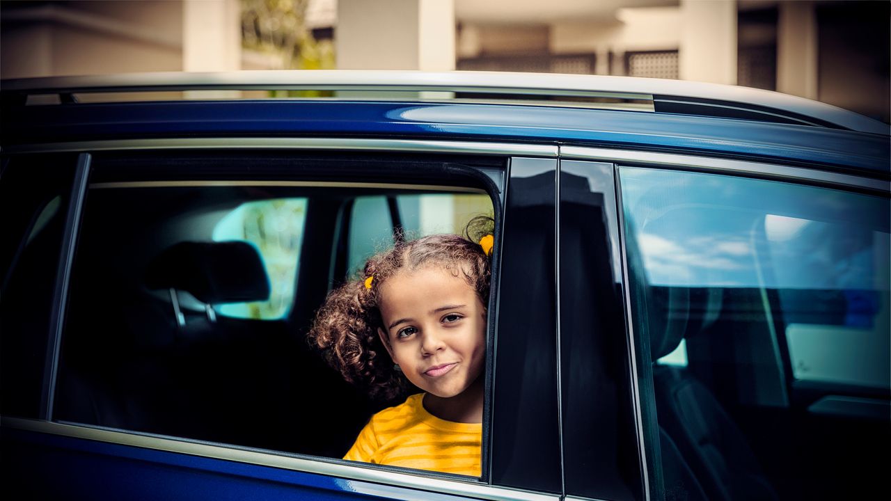 A child in a blue Volkswagen SUV looking out of the passenger window.