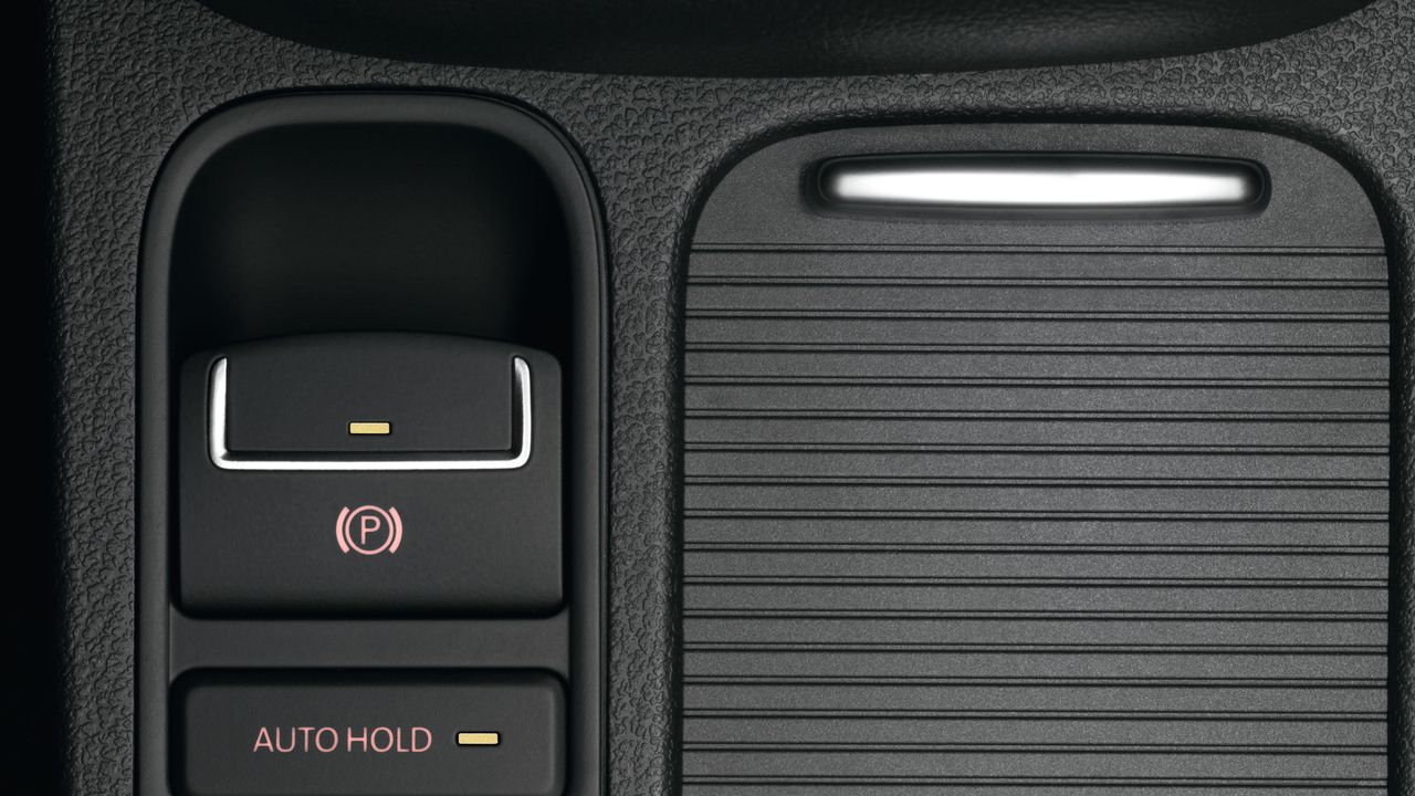 A close up look featuring the electronic parking brake and Auto Hold being switched on for a Volkswagen vehicle at its central console area.