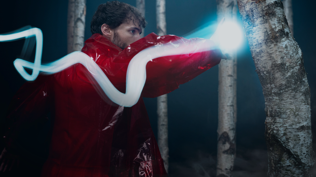 An individual dressed in striking red outfit is seen punching a tree in a studio setting.