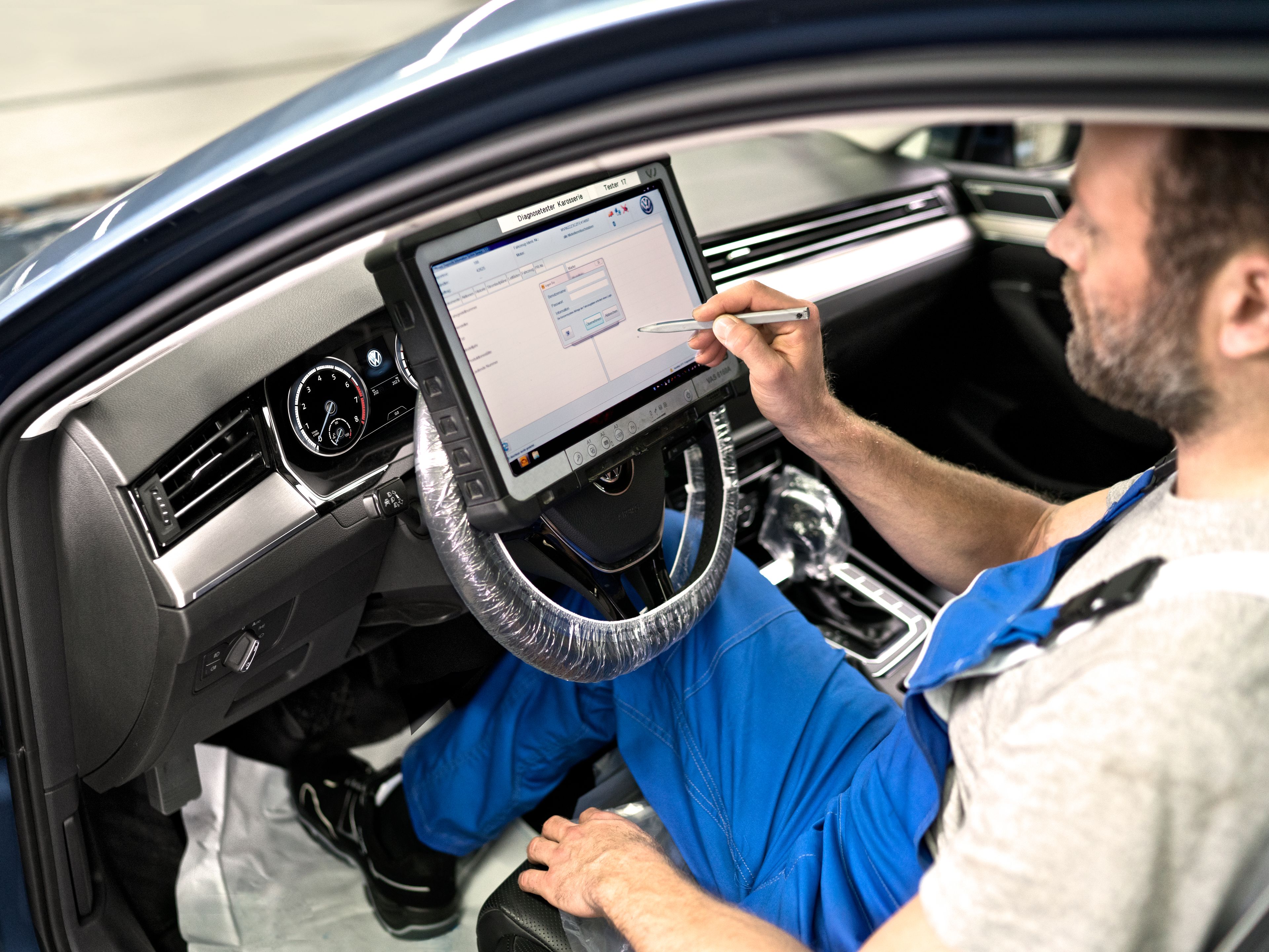 A Volkswagen technician inspecting a Volkswagen vehicle by utilising a diagnostic device to check for any abnormalities.