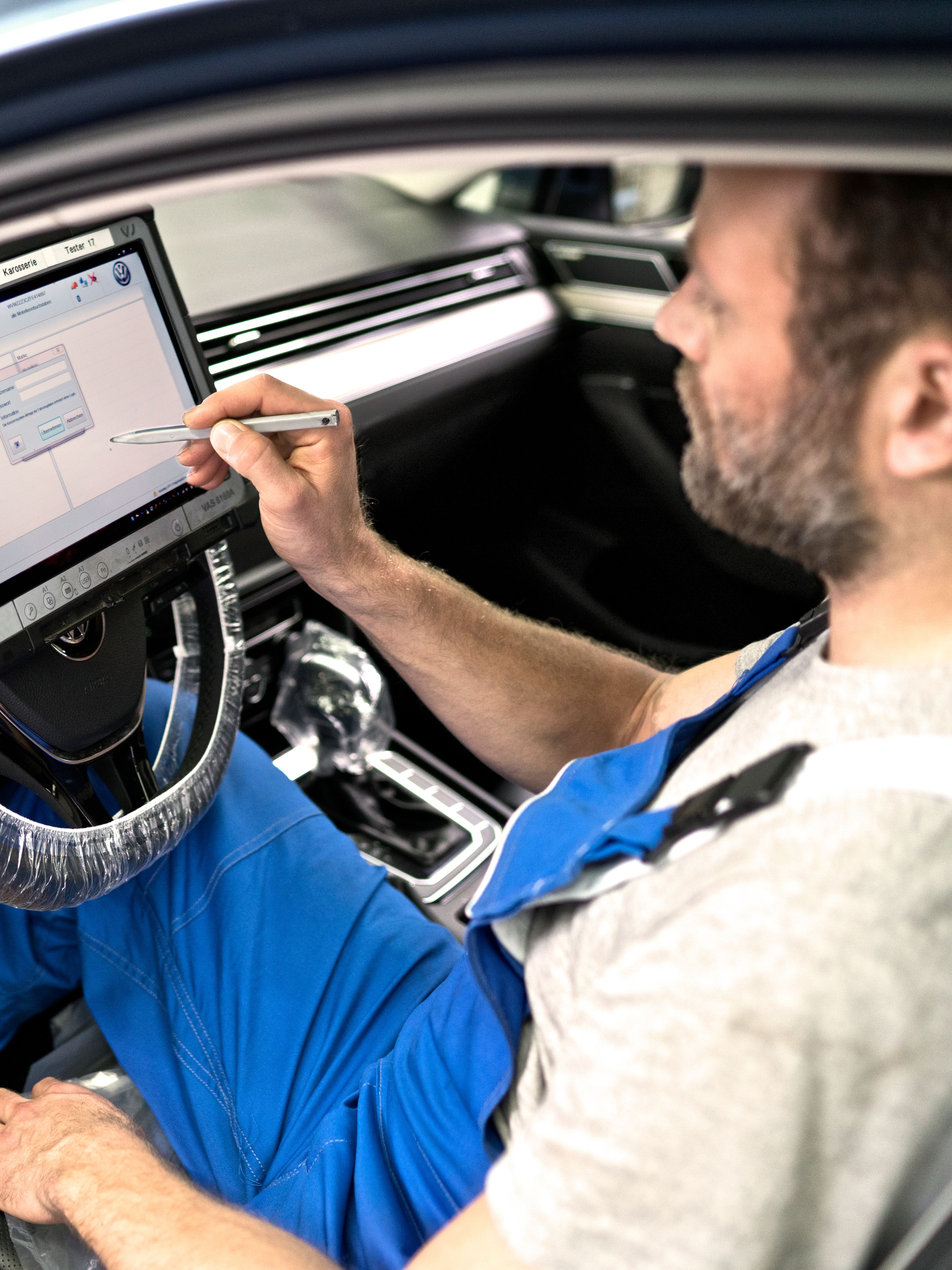 A Volkswagen technician inspecting a Volkswagen vehicle by utilising a diagnostic device to check for any abnormalities.