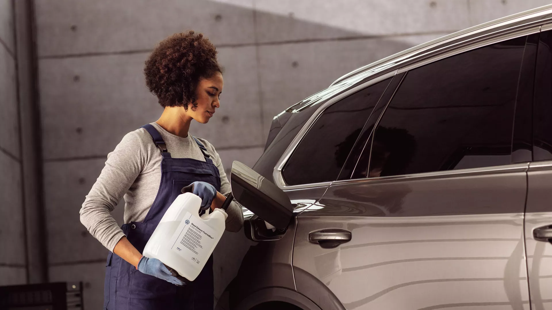 A Certified Volkswagen Staff pouring Volkswagen AdBlue® into a brown Volkswagen SUV.