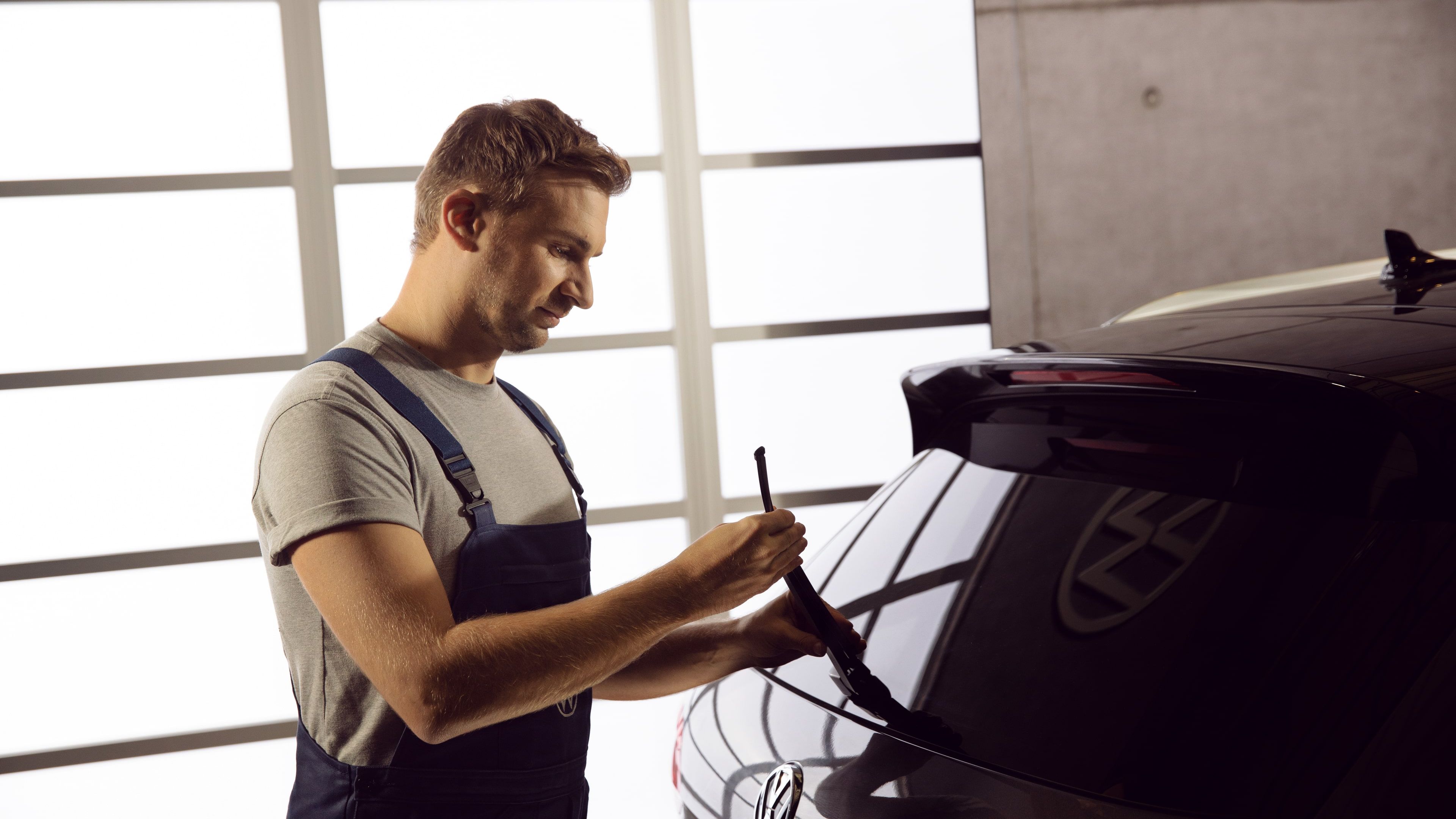 A Certified Volkswagen Staff assessing the condition of the Volkswagen Genuine Aero Wipers installed on a blue Volkswagen vehicle.