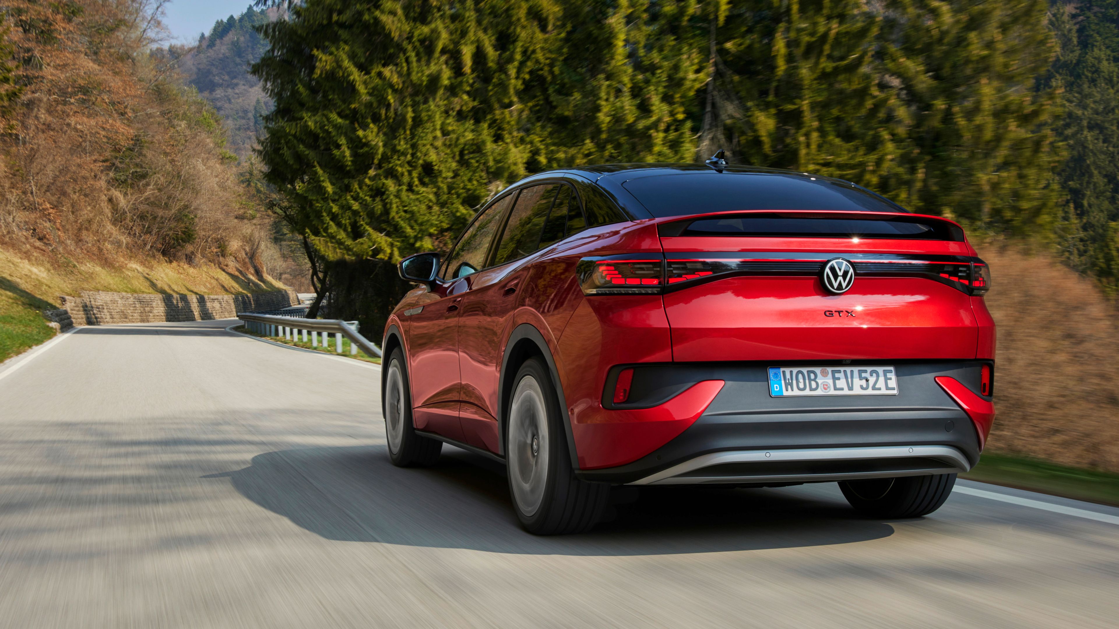 A Volkswagen ID.5 GTX is driving fast over the road surrounded by tall trees