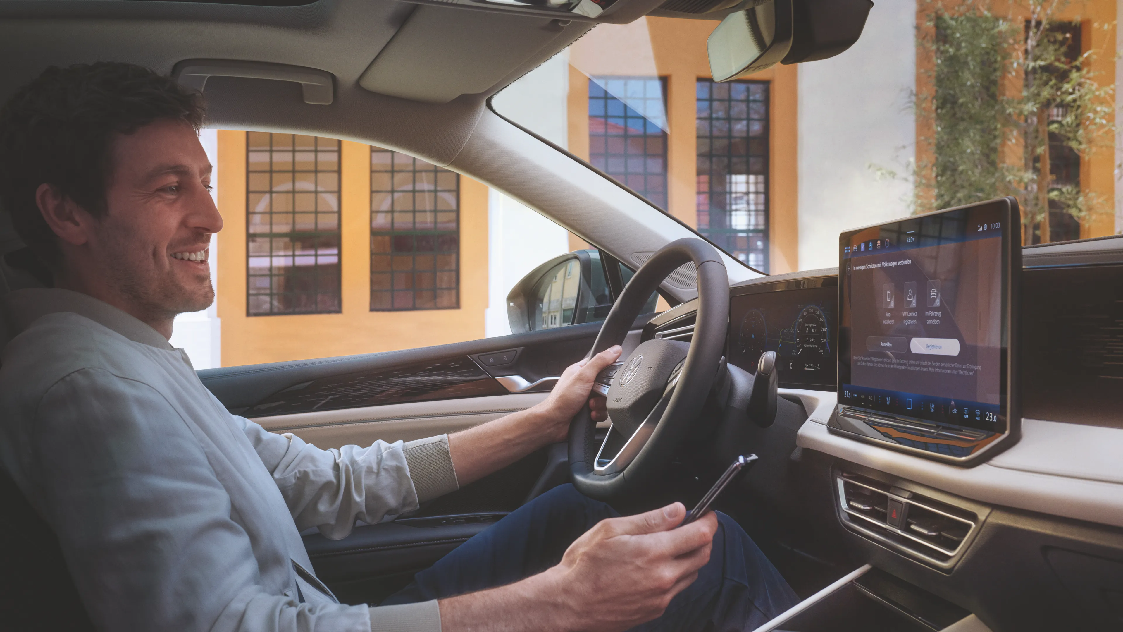 A man is seen using his smartphone in an idle Volkswagen Tiguan at day.